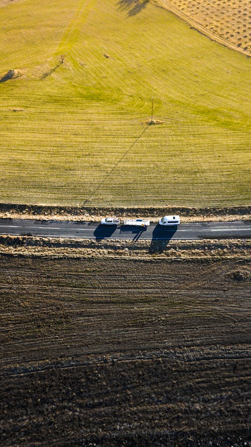 Aerial View of Camper Vans Driving on a Road Between Fields 