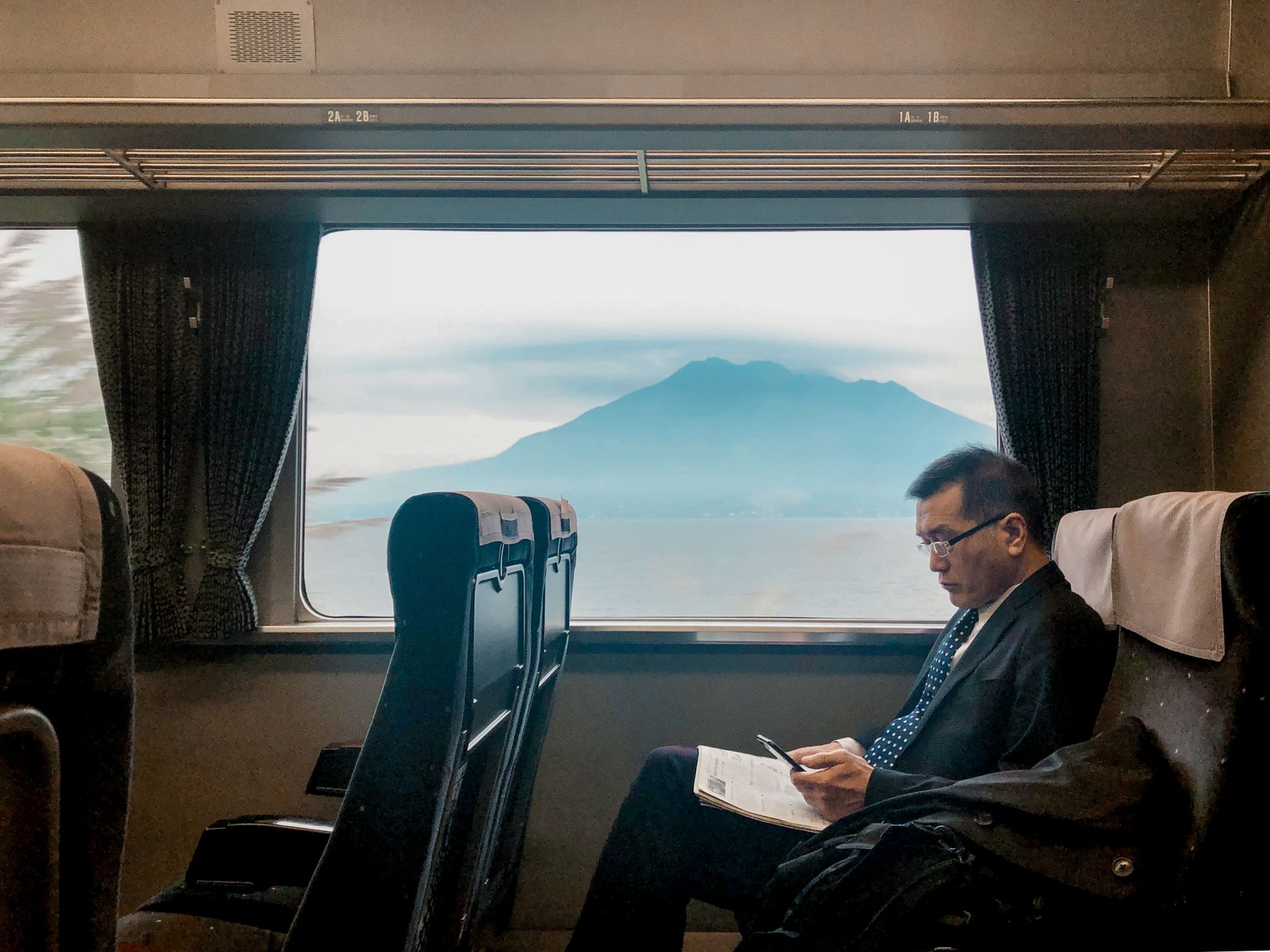 A man sitting on a train reads while Mount Fuji is visible through the window.