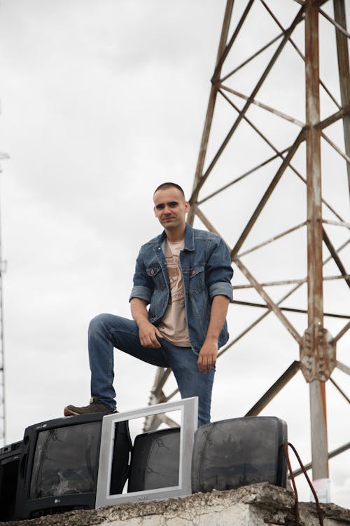 Man Standing on a Junkyard Resting His Leg on Old TVs 