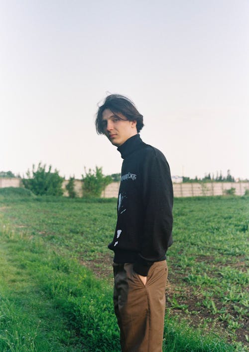 A Man in Turtle Neck Long Sleeves Standing on a Green Field while Looking at the Camera