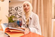 A Beautiful Woman Wearing Hijab Holding an Open Book while Smiling at the Camera