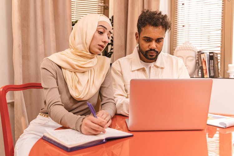 A Man And A Woman Sitting Beside Each Other While Looking At The Screen Of The Laptop