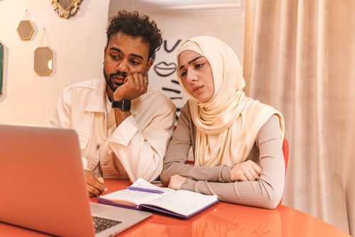 Free A man and woman in a cozy room focus on a laptop for a collaborative project, surrounded by warm decor. Stock Photo