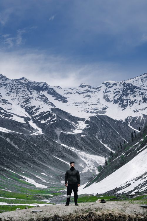 Free A hiker stands in a snow-capped mountain landscape under a clear blue sky. Stock Photo