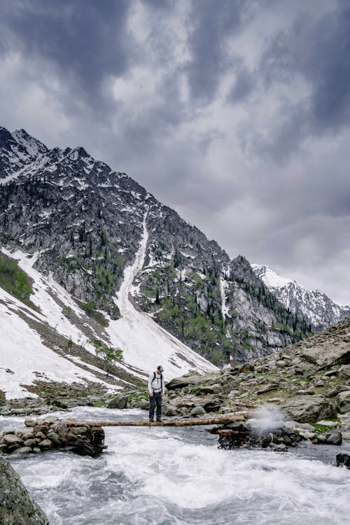 Man Standing on Tree Trunk over River in Mountains in Winter