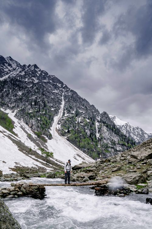 Free A person hiking along a river in a snowy mountain landscape, capturing the essence of outdoor adventure. Stock Photo
