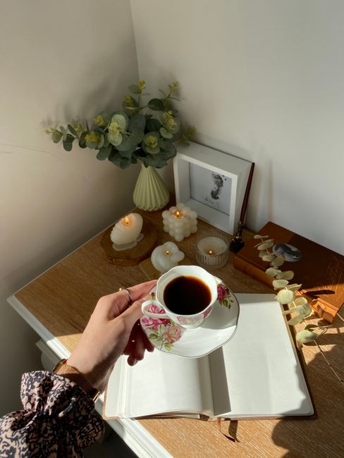 Warm morning setup with coffee, open notebook, and decorative candles on a wooden desk.