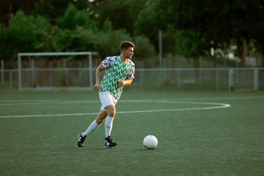 Soccer player in a green jersey dribbles a ball on an outdoor field during the day.