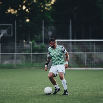 Soccer player with tattoos dribbling a ball on an outdoor field with goal post.（イメージ）