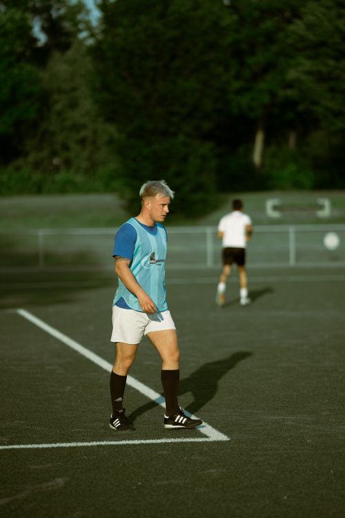 Free A young male athlete in a blue training vest walks on a soccer field during practice outdoors. Stock Photo