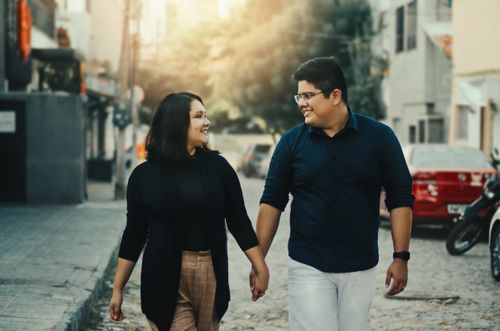 Free A happy couple holding hands and smiling at each other while walking down an urban street. Stock Photo