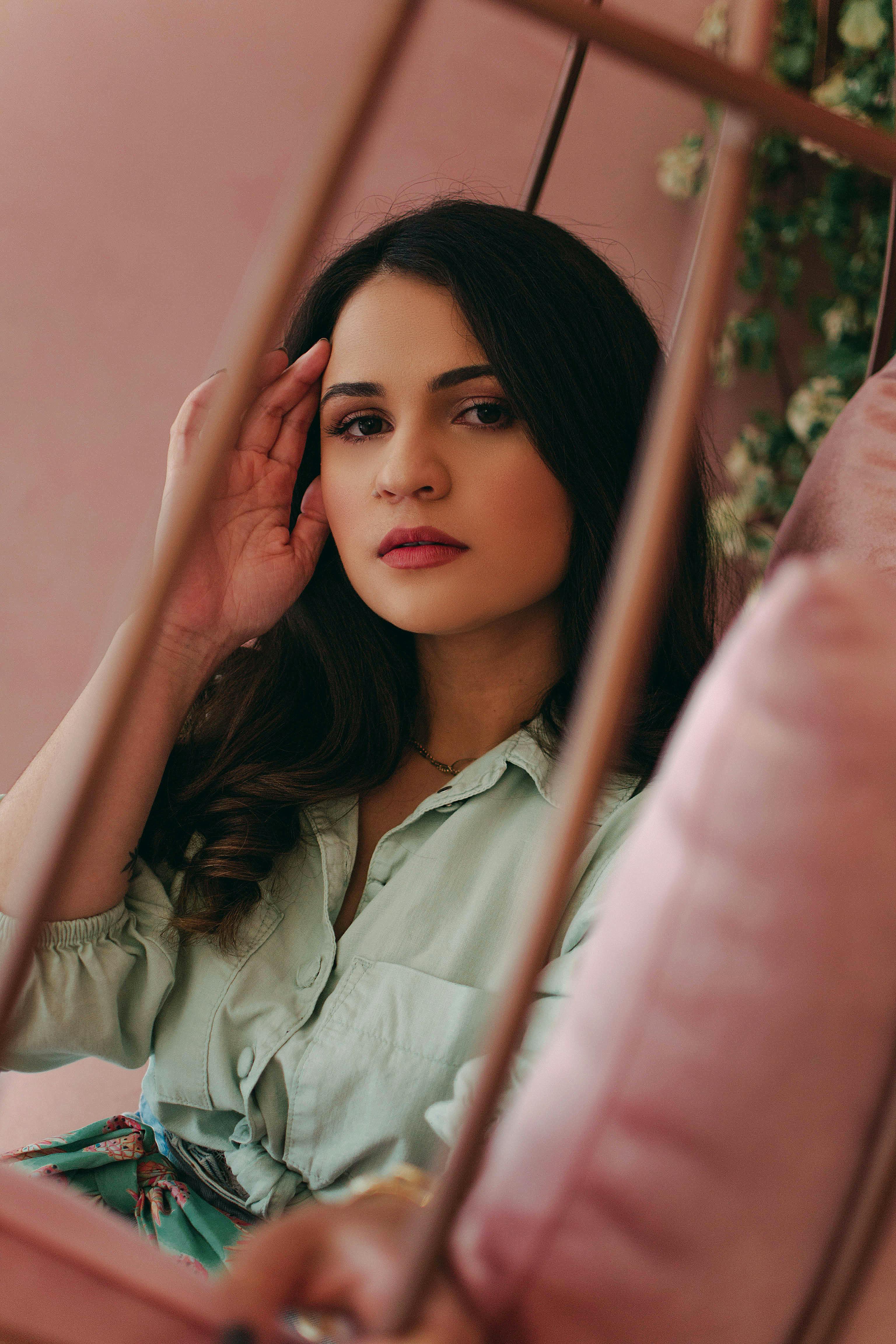A serene portrait of a woman in a green shirt posing against a soft pink background, creating a warm and inviting atmosphere.