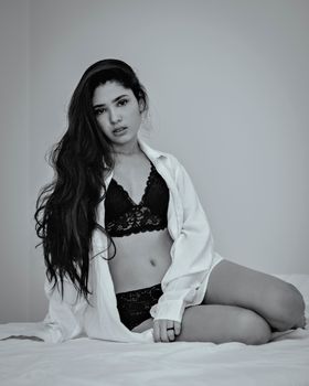 Artistic black and white portrait of a woman in lingerie sitting elegantly on a bed.