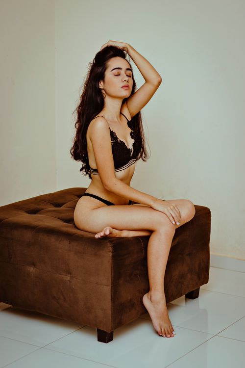 Free An adult woman in lingerie seated on a brown ottoman indoors with closed eyes. Stock Photo