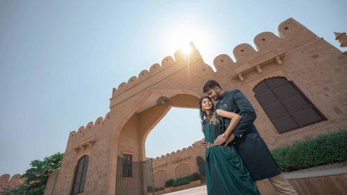 Free A happy couple in traditional clothes posing under a sunlit archway, embracing joyfully. Stock Photo