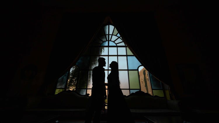 Silhouette Of Man And Woman Standing In Front Of Window