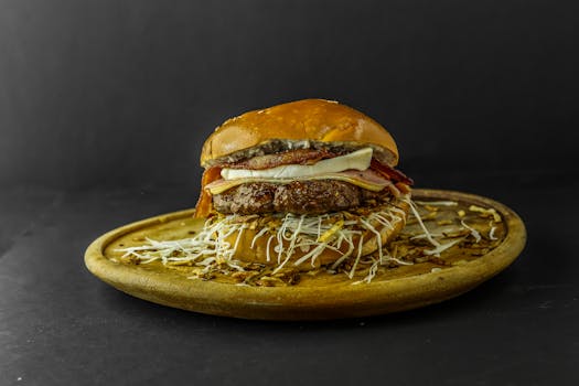 A delicious cheeseburger topped with bacon and onions, served on a rustic wooden plate.