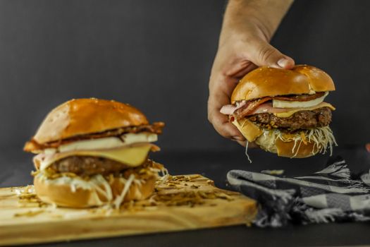 Close-up of two delicious bacon cheeseburgers, one being held, with melted cheese and fresh toppings.