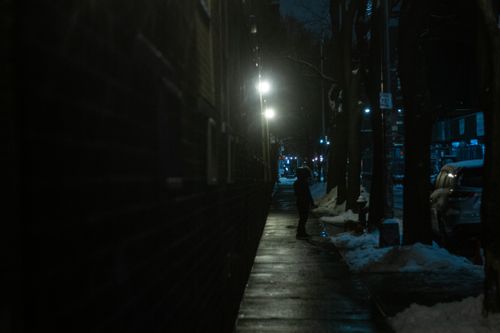 Free Unrecognizable citizen waiting and looking away on snowy empty asphalt sidewalk in downtown under light of streetlamp at cold winter evening Stock Photo