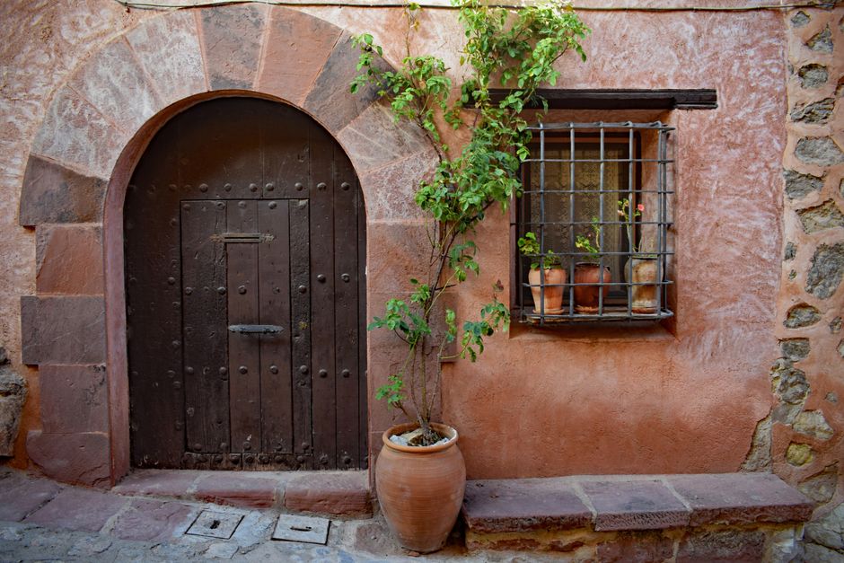 Charming rustic doorway with potted plants and wooden door in Albarracín, Spain.