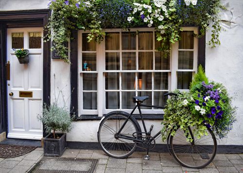 Free A vintage bicycle adorned with beautiful flowers parked outside a quaint guesthouse window. Stock Photo