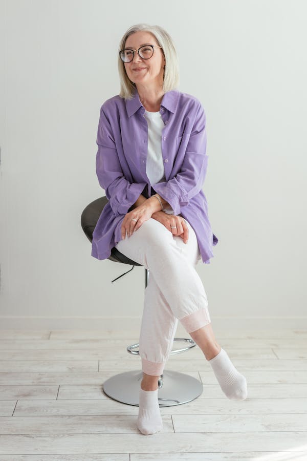 Woman in Purple Long Sleeve Shirt and White Pants Sitting on Chair