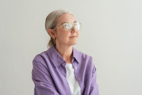 Free Senior woman with grey hair wearing eyeglasses and a purple shirt, looking thoughtful. Stock Photo