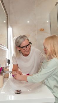 A joyful moment between a grandmother and granddaughter washing hands in a bathroom.