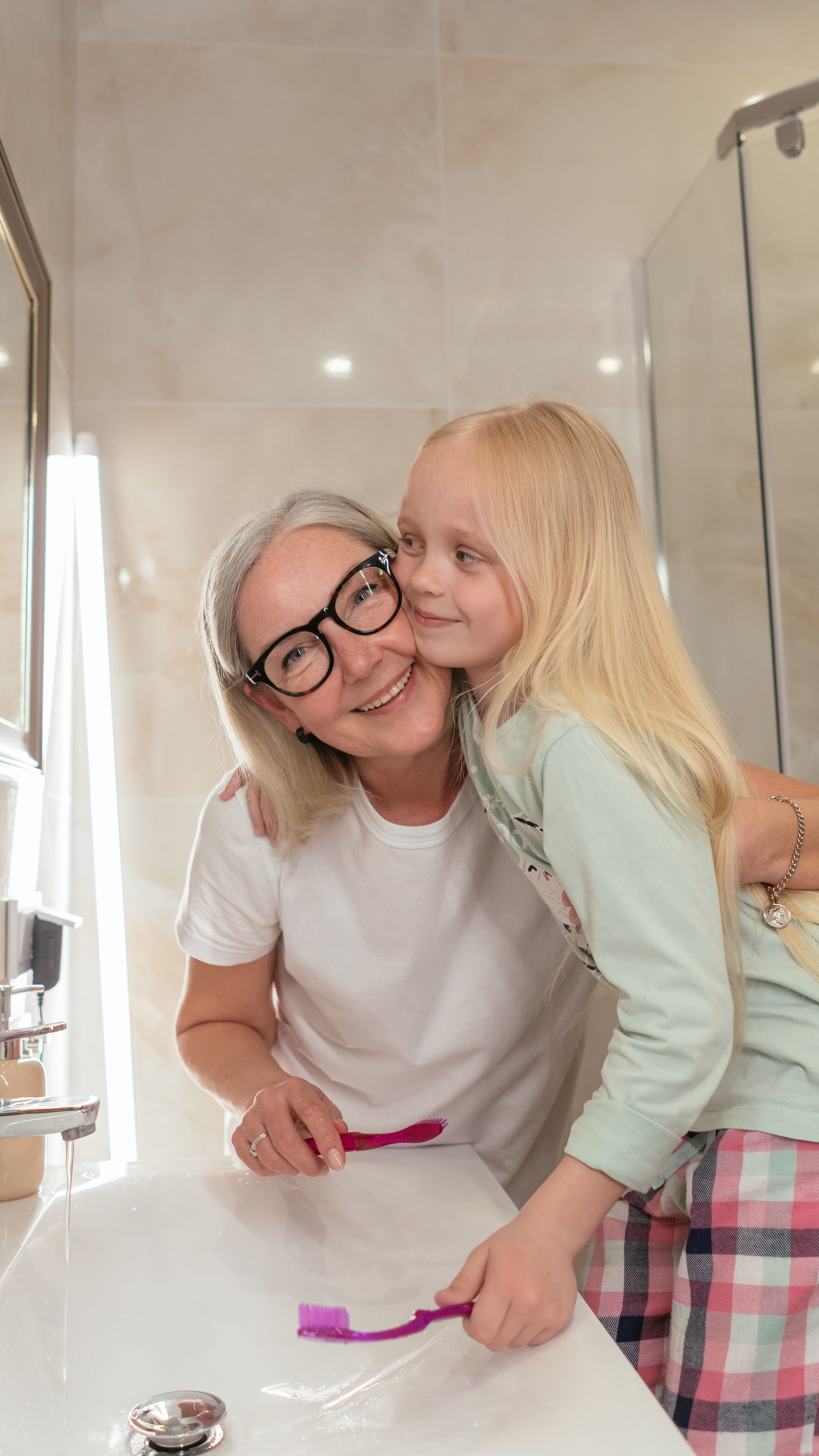 A joyful moment between grandmother and granddaughter brushing teeth together.