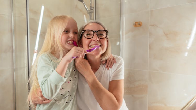 A Woman And Her Granddaughter Brushing Their Teeth Together