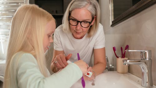 Free Grandmother Teaching her Granddaughter How to Brush her Teeth Stock Photo