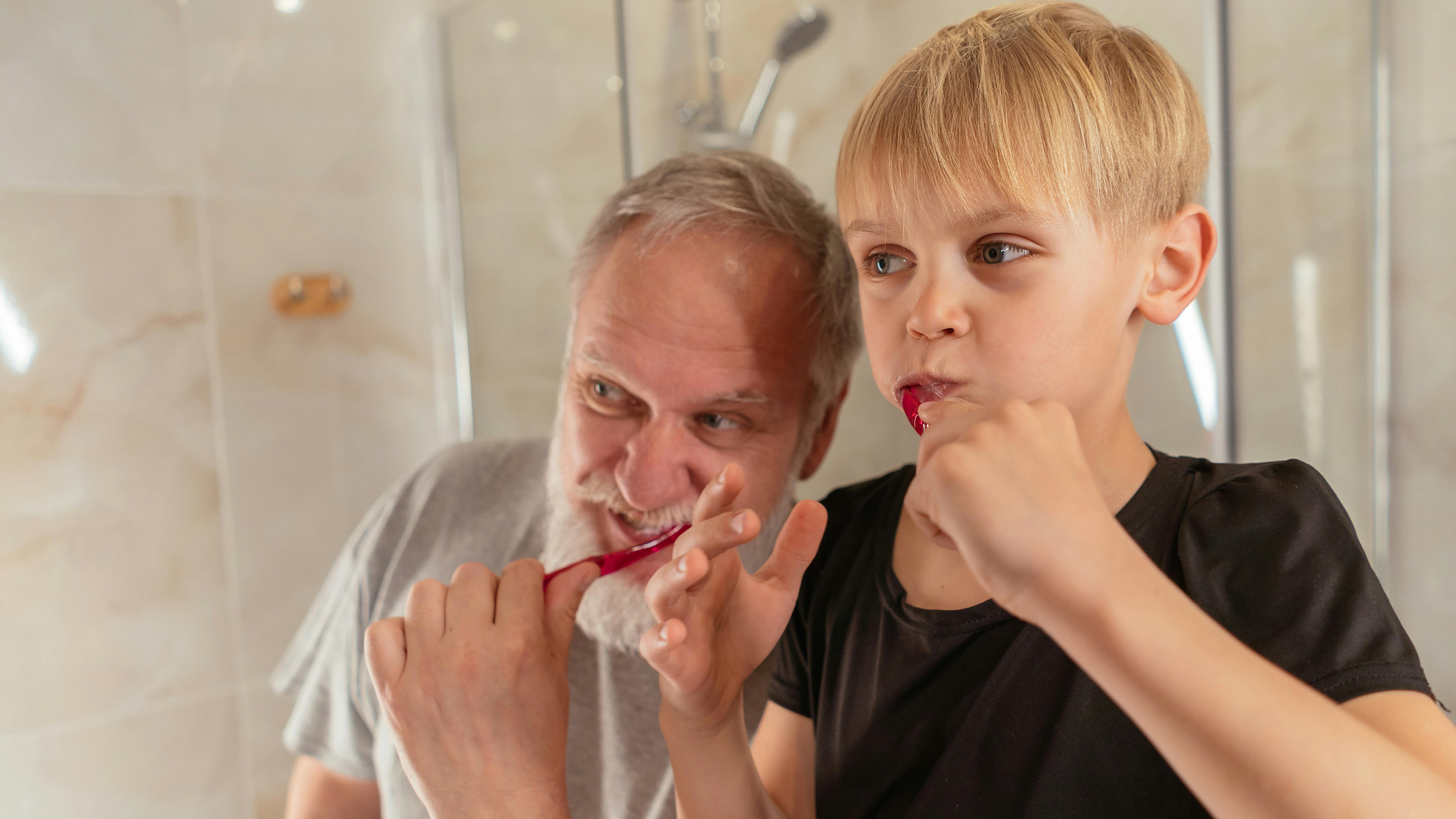 an elderly man brushing his teeth with his grandson