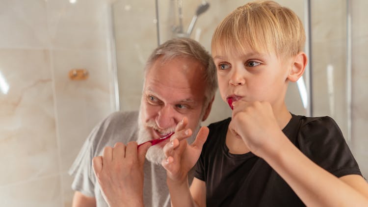 An Elderly Man Brushing His Teeth With His Grandson