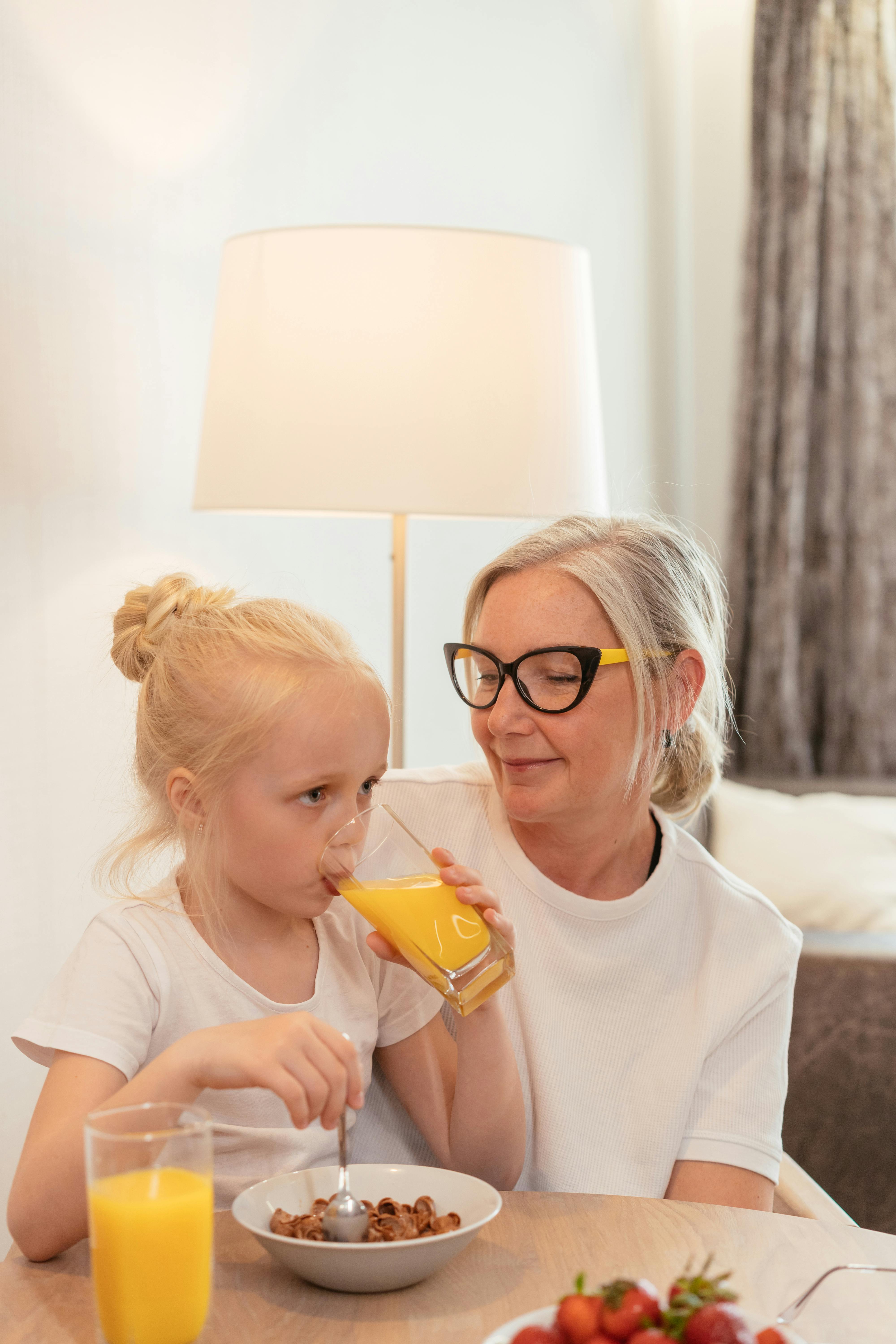 cute girl sitting with her grandmother while drinking orange juice