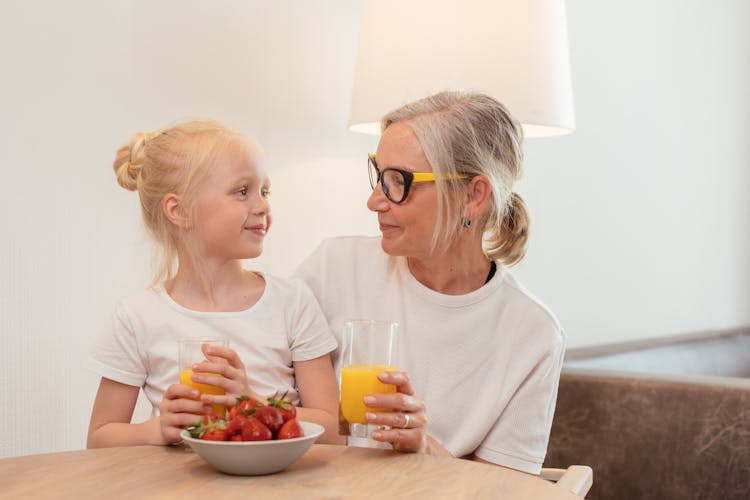 Elderly Woman Sitting With A Girl Drinking Orange Juice