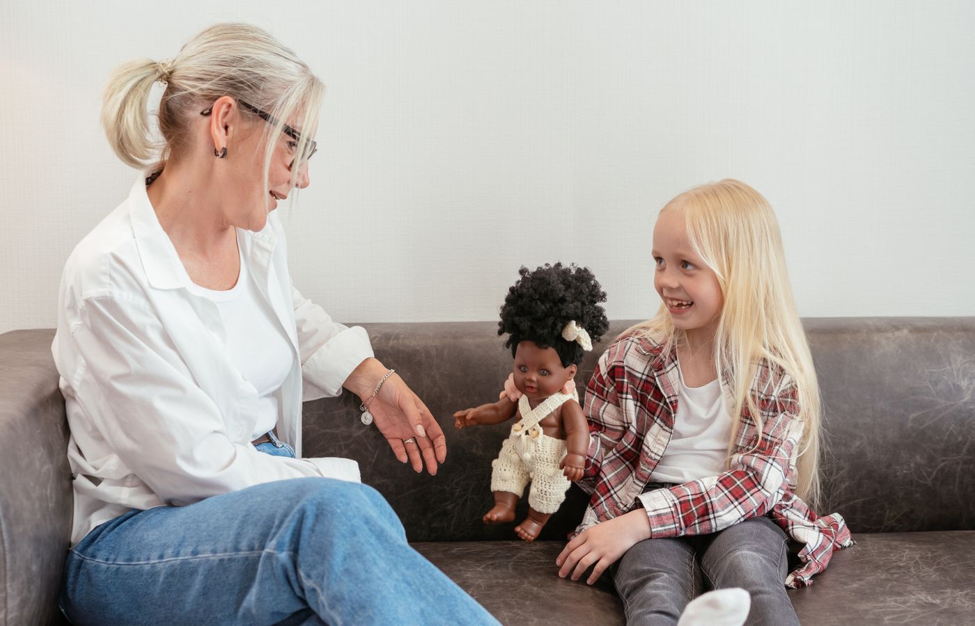 A grandmother and granddaughter enjoy quality time together on a couch with a doll.