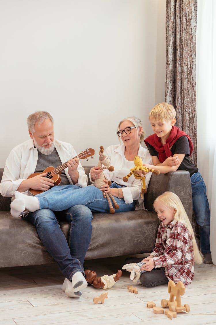 Grandparents Sitting On Sofa Playing With Their Grandchildren