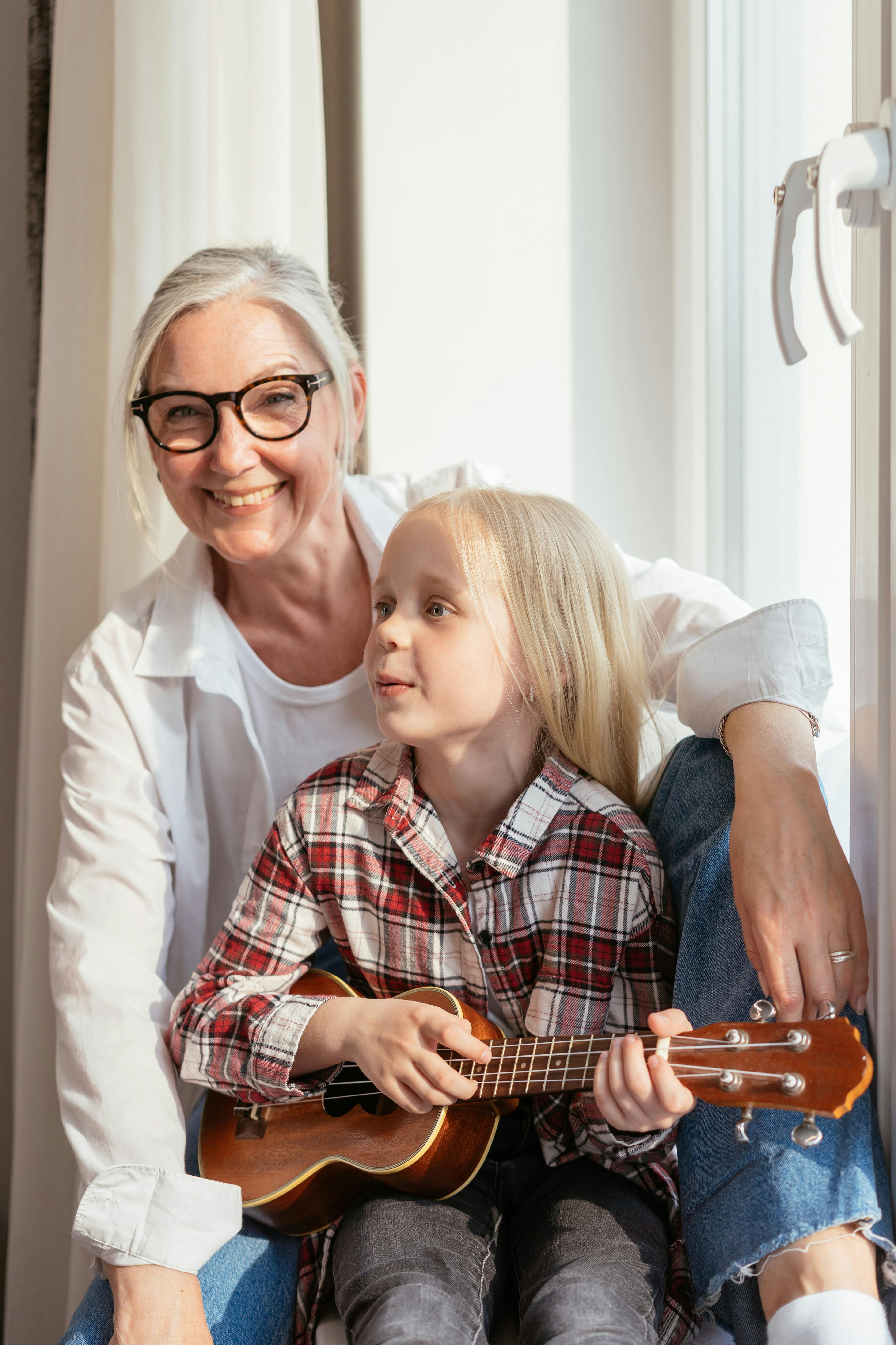 an elderly woman sitting near her granddaughter playing ukulele