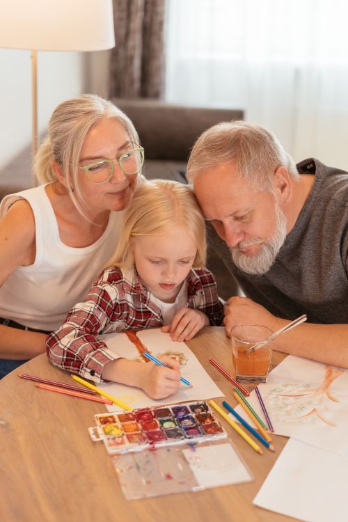 Free A child painting with grandparents at home, showcasing family and creativity. Stock Photo