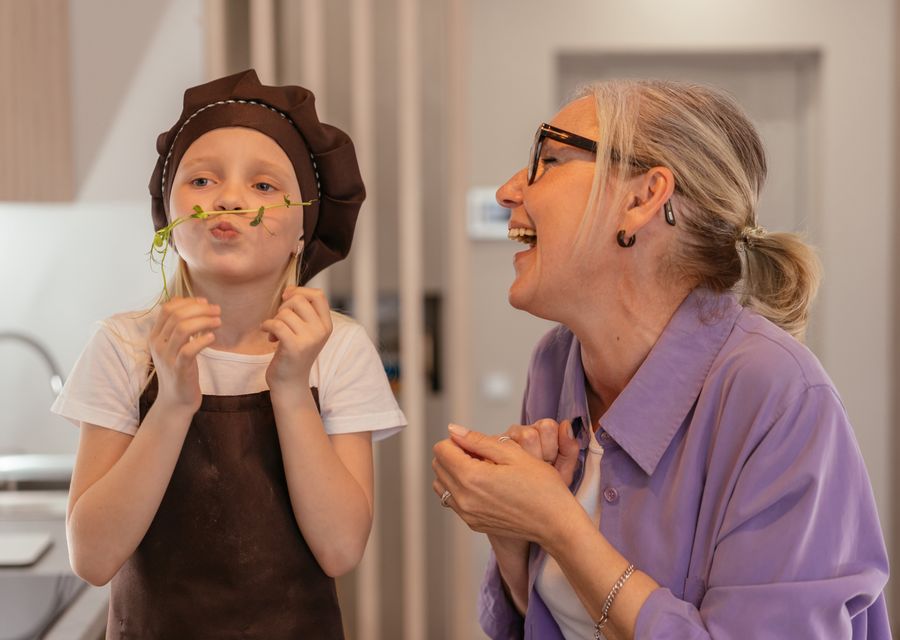 A senior woman and her young grandchild cooking together, laughing.
