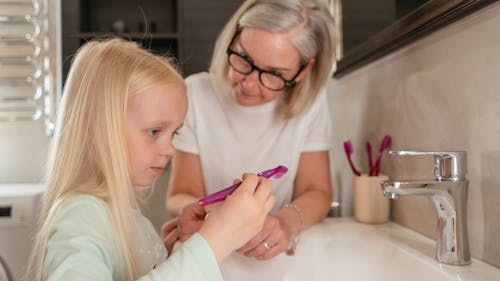 Woman Beside a Girl Holding Pink Toothbrush 