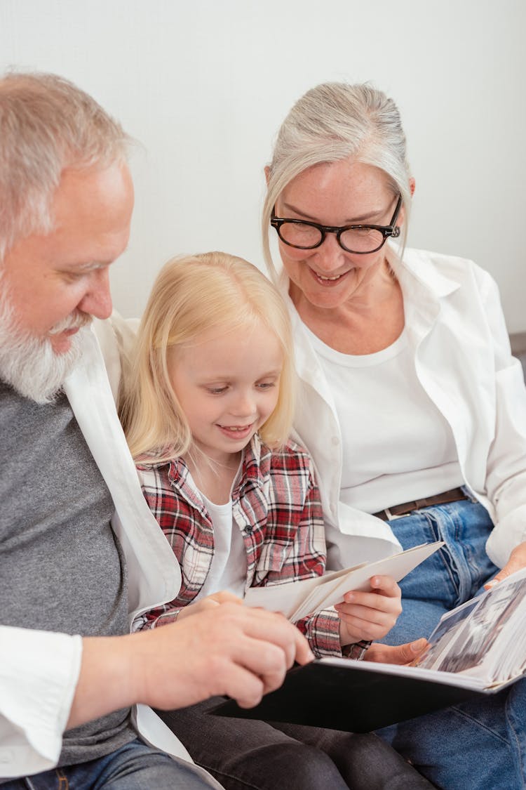 A Young Girl Looking At The Photo Album With Her Grandparents