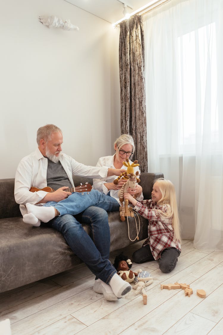 Elderly Couple Sitting On Sofa Playing With Their Grandchild