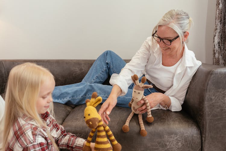 An Elderly Woman Sitting On The Couch While Playing With Her Granddaughter