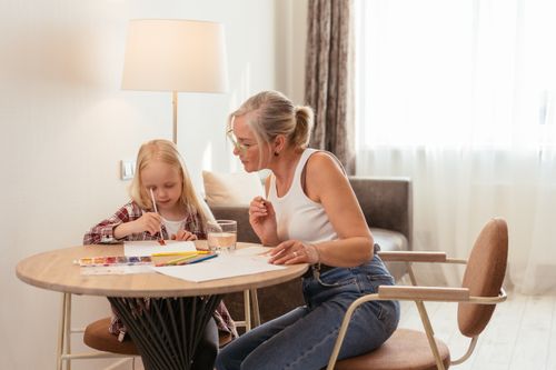 Free A grandmother and her grandchild enjoy painting together at a table in a cozy indoor setting. Stock Photo