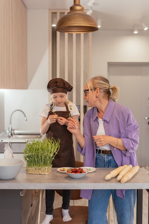 Woman in Purple Dress Shirt Cooking with Girl in Brown Apron