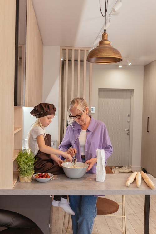 Woman in Purple Dress Shirt Cooking with Girl in Brown Apron