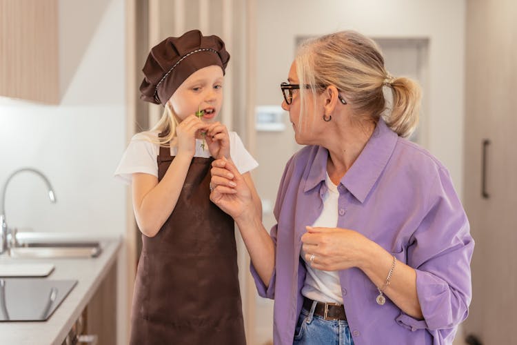 Grandmother Looking At The Kid Wearing Apron While Eating Vegetables