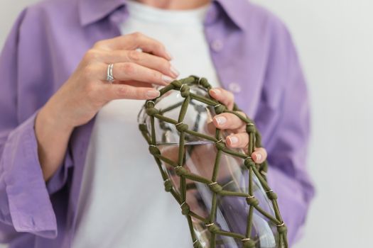 Woman's hands holding a bottle in a knotted cover. Close-up, indoors.