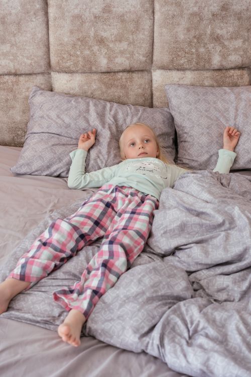Free A young child wearing pajamas relaxes on a comfortable bed, enjoying a cozy indoor atmosphere. Stock Photo